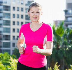 Athletic female in pink T-shirt is jogging around the urban.