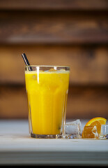 Fresh orange juice with crushed ice and straw on table with wood background