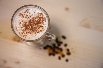 Cappucino with cinamon in tall glass from above on table with wood background and coffee beans