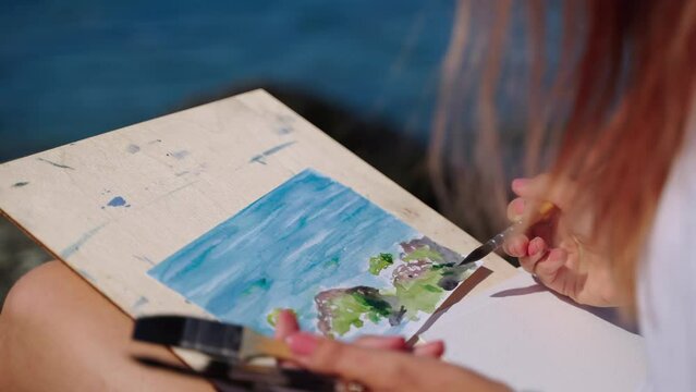 Woman spending free time with watercolor painting by the sea