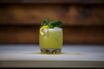 Fresh cold lime smoothie cocktail with mint and crushed ice and lemon twist to garnish on table with wood background