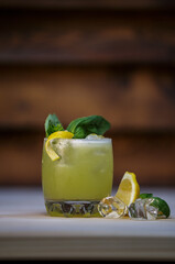 Fresh cold lime smoothie cocktail with mint and crushed ice and lemon twist to garnish on table with wood background