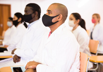 Portrait of young adult male doctor attentively listening to lecture with colleagues, medical conference during coronavirus pandemic
