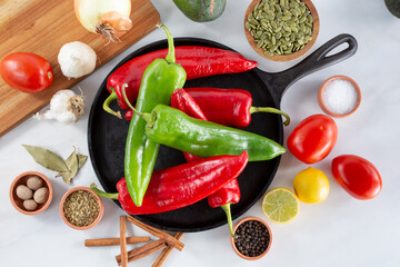 A top down view of a comal full of red and green Anaheim chiles, among other salsa ingredients.