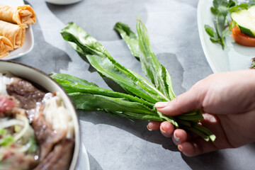 A view of a hand holding several culantro leaves.