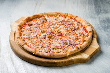 Pizza with tuna and red onion on the board on grey table