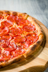Pepperoni pizza on wooden board on grey table macro close up vertical
