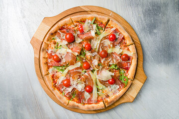 Pizza with Parma ham, greens and parmesan on wooden board on grey table top view - obrazy, fototapety, plakaty