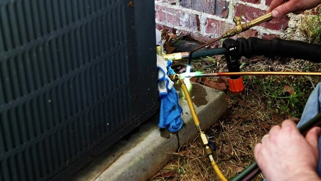 Maintenance worked uses and oxygen Acetylene torch to braze copper tubing on an air conditioner system
