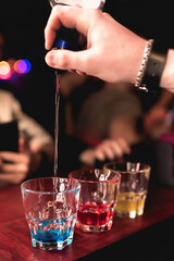 The bartender prepares colorful cocktails in the bar. Bartender's hand close up