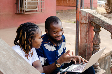 two young african friends, male and female watching movie with a laptop