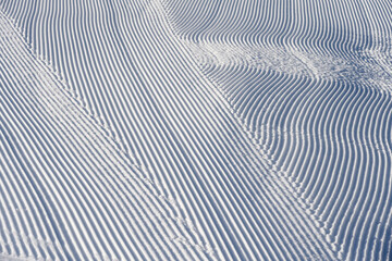 Fototapeta na wymiar Fresh snowfall after the groomers have finished rolling the ski slopes, pattern and texture in a natural cold white snow background 
