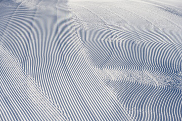 Obraz na płótnie Canvas Fresh snowfall after the groomers have finished rolling the ski slopes, pattern and texture in a natural cold white snow background 