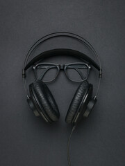 Black headphones and classic black glasses on a black background. Flat lay.
