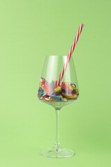 A large glass with sweets and a cocktail tube on a green background.