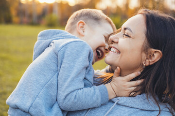 Fototapeta premium The mother walking through the autumn park with her son in her arms, telling the child something funny. Smiling happy child. Happy people. Family care. Close-up