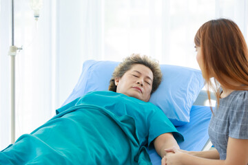 Obraz premium Old senior Asian sick illness mother patient in hospital uniform lay down sleeping on bed receive saline solution infusion while young worry woman daughter visiting holding hands with love and care