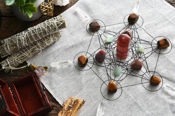 A top view image of a crystal healing grid using sacred geometry with white sage smudge bundles. 