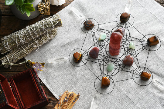 A top view image of a crystal healing grid using sacred geometry with white sage smudge bundles. 