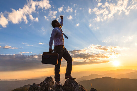 Successful business man, holding his business attache and standing on top of mountain goldden color sunset background,  this photo conveys the message of success, competition and leadership concept.