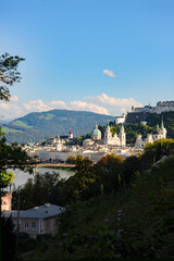 A postcard view of Salzburg, Austria with the Fortress Hohensalzburg perched high above the city skyline with endless views of pristine mountains and bluest of blue skies.