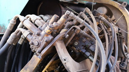Old hydraulic valves and hoses. Close-up of pumps and valves connecting dusty mini excavator...