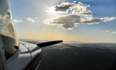 Flying a small airplane in a beautiful landscape with spectacular sky. View outside of the plane, with the front part and the propeller in frame. Aviation industry.
