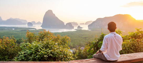 Fototapeta na wymiar Happy traveler man enjoy Phang Nga bay view point, alone Tourist sitting and relaxing at Samet Nang She, near Phuket in Southern Thailand. Southeast Asia travel, trip and summer vacation concept