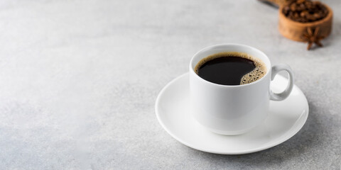 Black coffee in a white mug on a saucer on a grey table. Copy space.