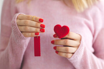 close up woman's hands with red manicure holds heart under wool pastel pink knitted sweater background I love you symbol Valentine's day