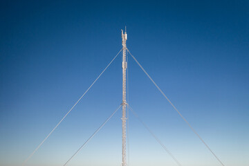 Fototapeta premium Frost covered telecommunications mast against blue sky in winter.