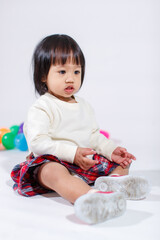 Studio shot of little cute short black hair Asian baby girl daughter model in casual plaid skirt sitting on floor smiling laughing playing with colorful round balls toy alone on white background