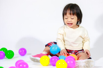 Fototapeta na wymiar Studio shot of little cute short black hair Asian baby girl daughter model in casual plaid skirt sitting on floor smiling laughing playing with colorful round balls toy alone on white background