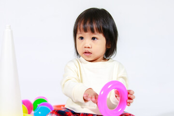 Studio shot of little cute short black hair Asian baby girl daughter model in casual plaid skirt sitting on floor smiling laughing playing with colorful round balls toy alone on white background