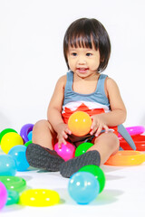 Fototapeta na wymiar Studio shot of little beautiful kindergarten Asian baby girl daughter model in cute gray shark costume swimsuit outfit sitting on floor with colorful plastic balls and rings toy on white background