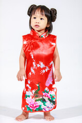 Studio shot of little cute innocent Asian kindergarten preschooler daughter girl kid model with bun hairstyle in red Chinese traditional qipao Cheongsam outfit standing alone on white background