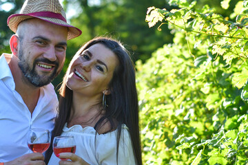 Fototapeta premium Portrait of a smiling happy couple kissing in a Vineyard toasting wine. Beautiful brunette woman and bearded muscular man spending time together during grape harvest.
