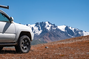 White SUV with snowy mountains on background. Off-road journey, travel concept.