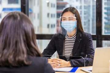 Manager from HR department wearing facial mask is interviewing new applicant and reading her resume...