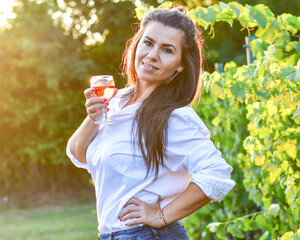 Young beautiful smiling woman  sitting with a cat in  a Vineyard with a glass of  rose wine. Woman playing with cat during the summer vacation