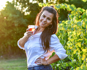 Young beautiful smiling woman  sitting with a cat in  a Vineyard with a glass of  rose wine. Woman playing with cat during the summer vacation