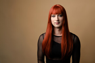  Portrait of young transgender woman in a red wig and makeup on a brown background. Concept diversity, transsexual, and freedom.