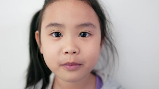 Asian girl holding a clear plastic cup drinking delicious milk using a straw, happy face, wide smile showing teeth. Close-up camera angle of face.