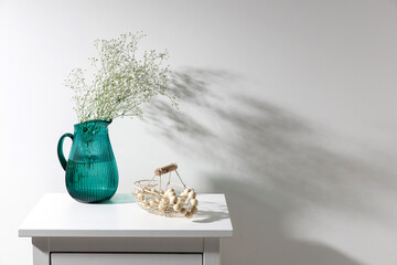 A large glass green jug with a bouquet of gypsophila and an iron basket with wooden beads on a...