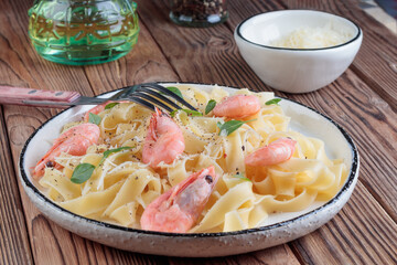 Close-up view of pasta fettuccine with shrimp in rustic plate with fork on wooden background. Soft focus.