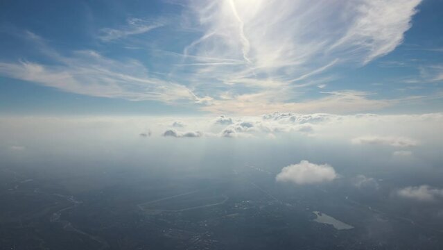 Aerial view from airplane window at high altitude of distant city covered with layer of thin misty smog and distant clouds
