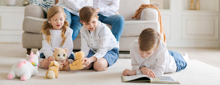Happy young caucasian family resting in a new cozy design home on weekends. Delighted parents resting in their own home, children have fun sitting on the floor with toys and a book