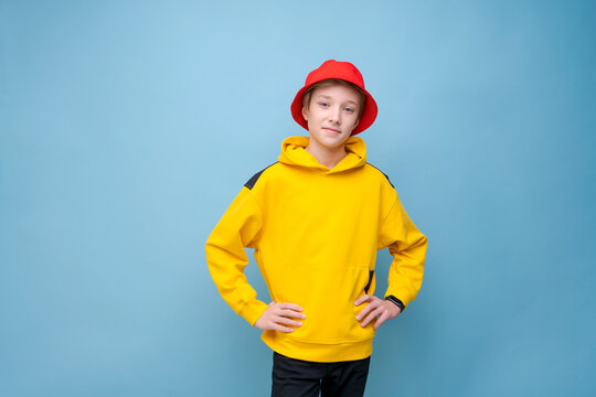 Portrait of positive guy in yellow jacket and a red panama hat on a blue background, looking at the camera with a smile on his face. Happy caucasian teenager posing in cute smiling studio