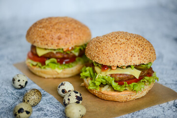 two large juicy fresh burgers on a light background with quail eggs on the table
