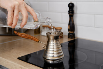 Closeup view of man pouring water into cezve with ground coffee